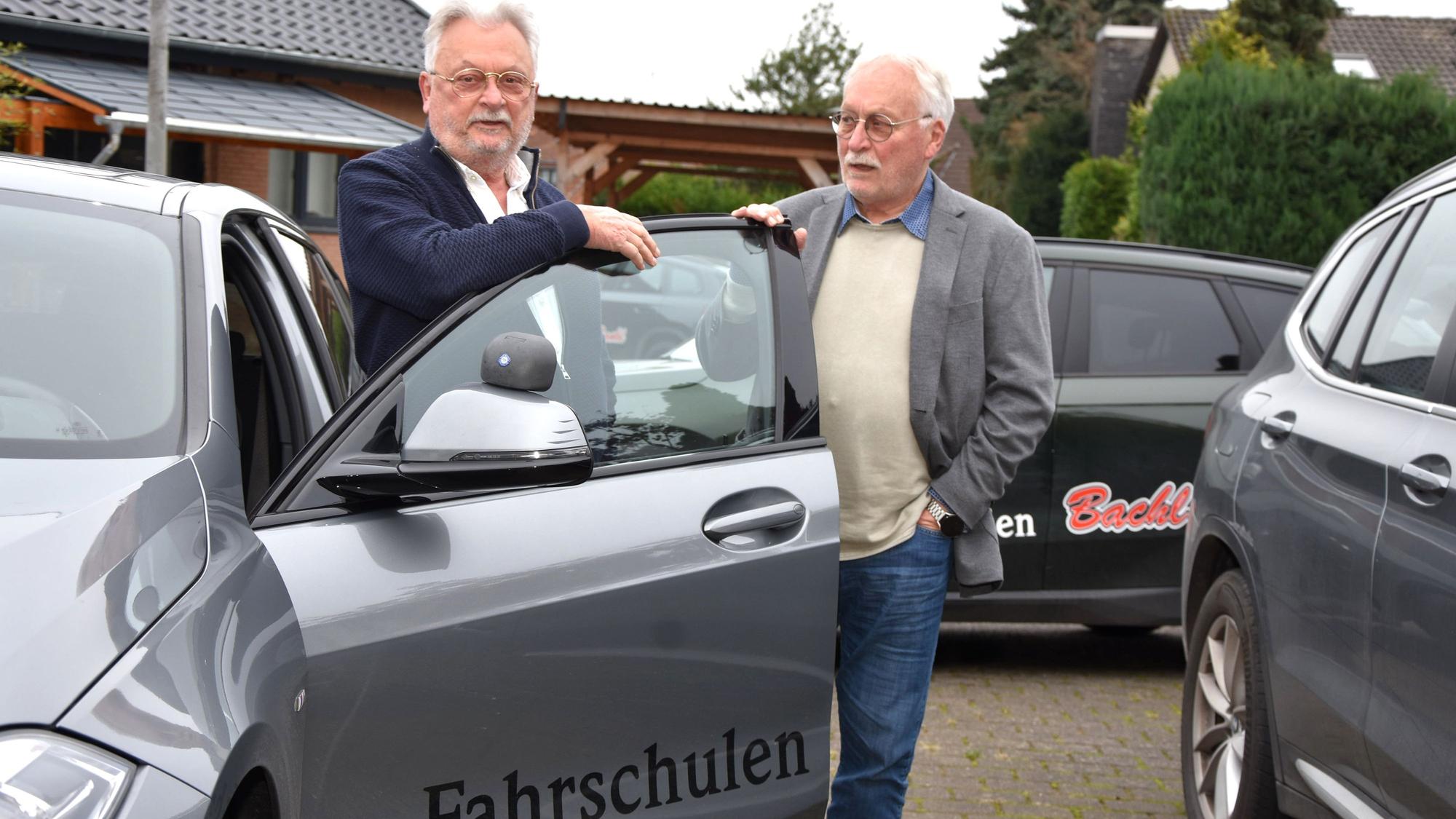 Zu sehen sind zwei Männer an einem Fahrschulauto.