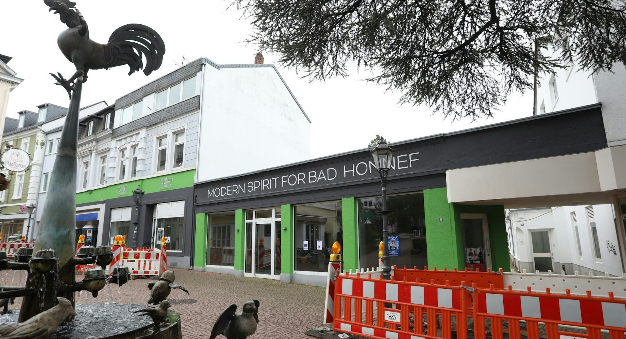 Eine Reihe von Geschäftshäusern mit leeren Ladenlokalen, am linken Rand steht ein Springbrunnen.