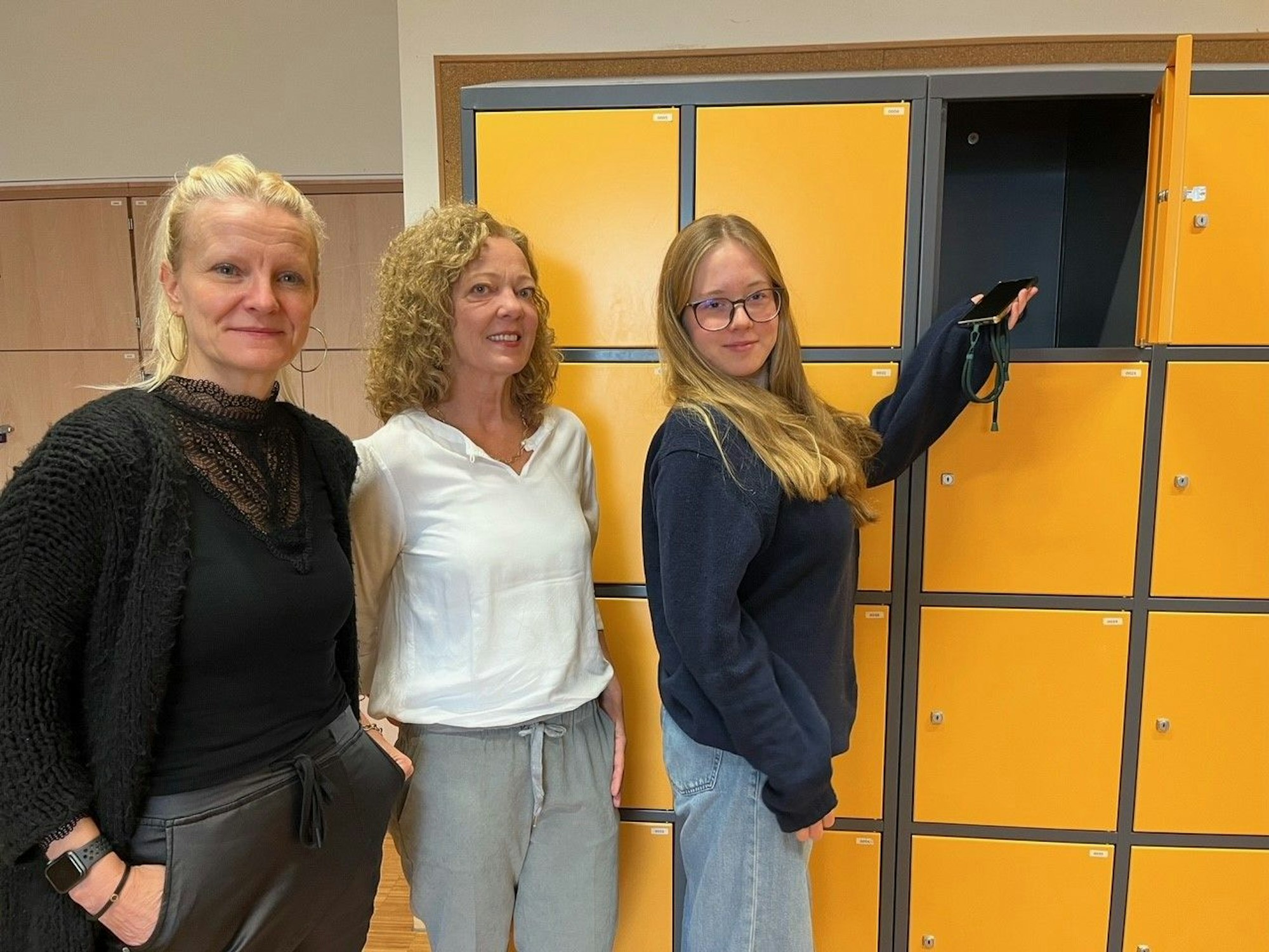 Drei Frauen stehen vor gelben Spinden.