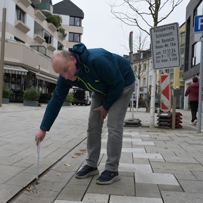 Der Schwiegersohn misst mit einem Zollstock den Höhenunterschied zwischen Bodenbelag und Pflasterstein.