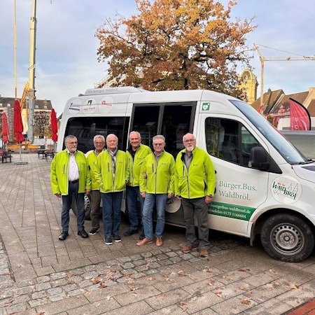 Rollt ab Montag, 4. August 2025, nur noch auf Bestellung per App oder Telefon durch die Marktstadt: der Waldbröler Bürgerbus. Auf dem Foto haben sich einige der Fahrer am Fahrzeug versammelt.