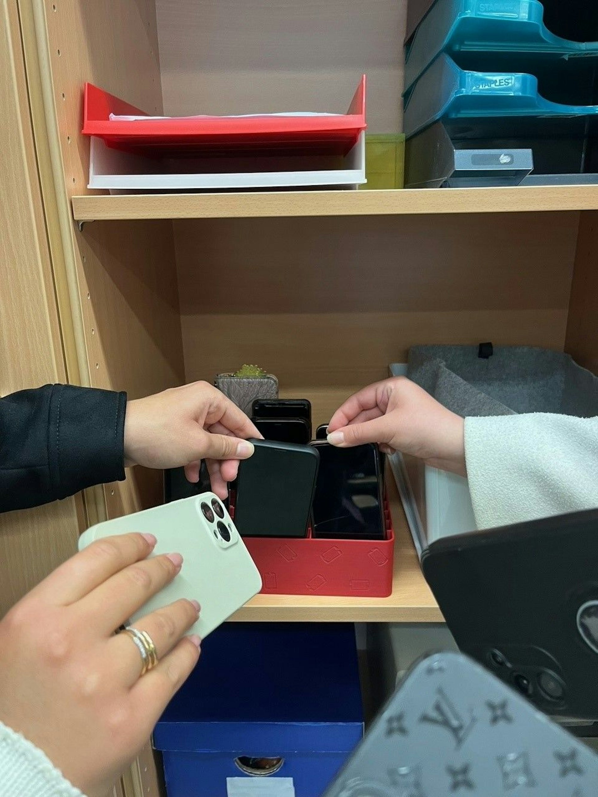 Hände verbringen Mobiltelefone in eigens für die Geräte bereitstehenden Boxen.