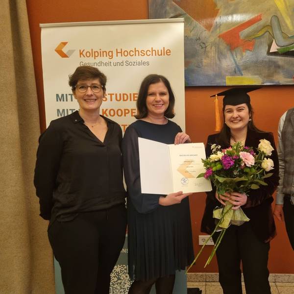 Vier Personen stehen in einer Reihe. Eine von ihnen hält einen Blumenstrauß in der Hand.