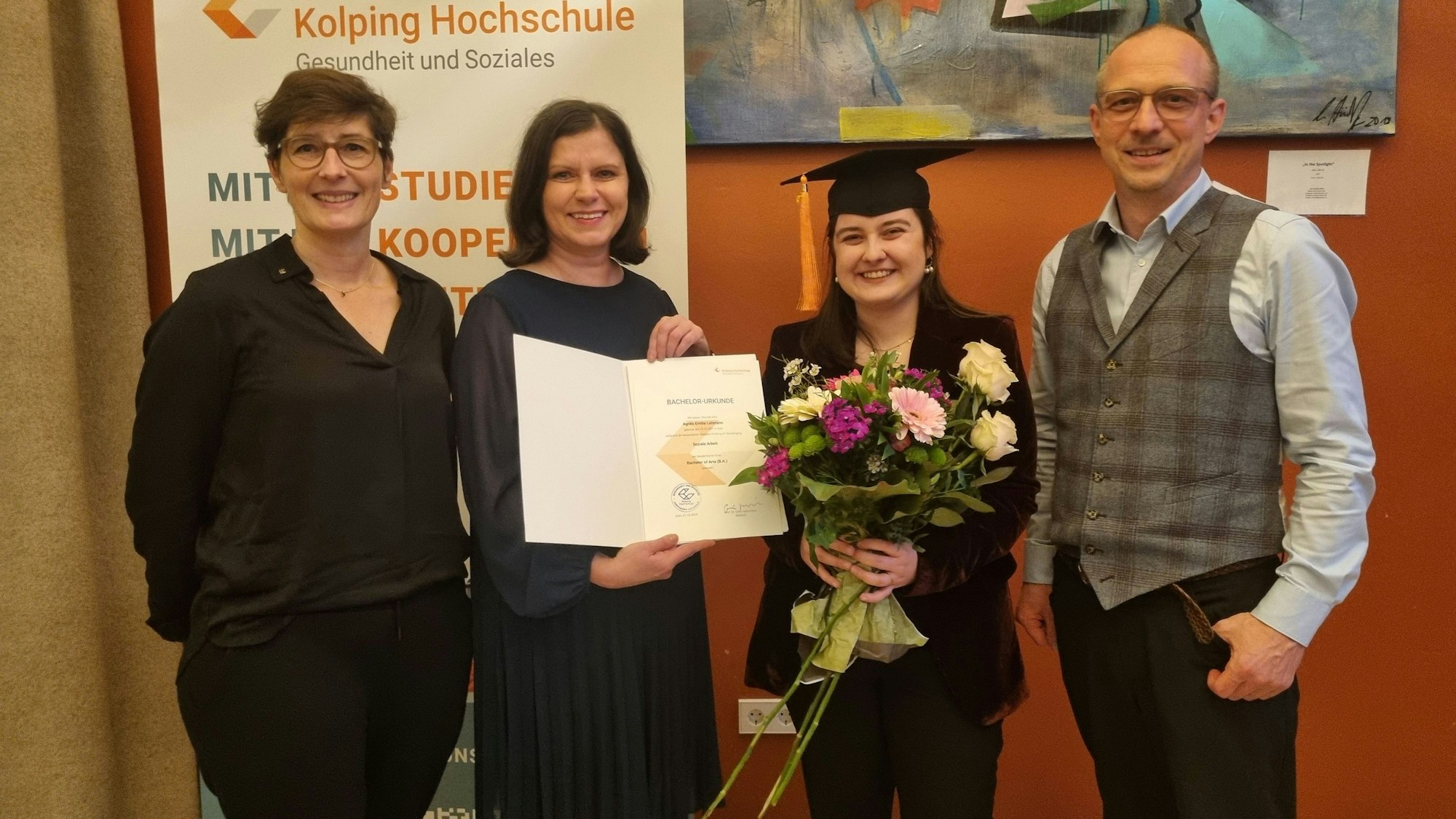 Vier Personen stehen in einer Reihe. Eine von ihnen hält einen Blumenstrauß in der Hand.