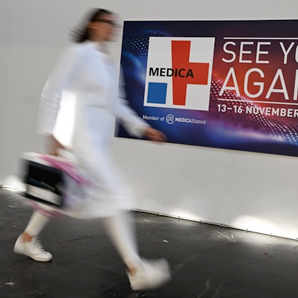 Eine Frau in weißem Kittel eilt an einem Medica-Plakat vorbei.