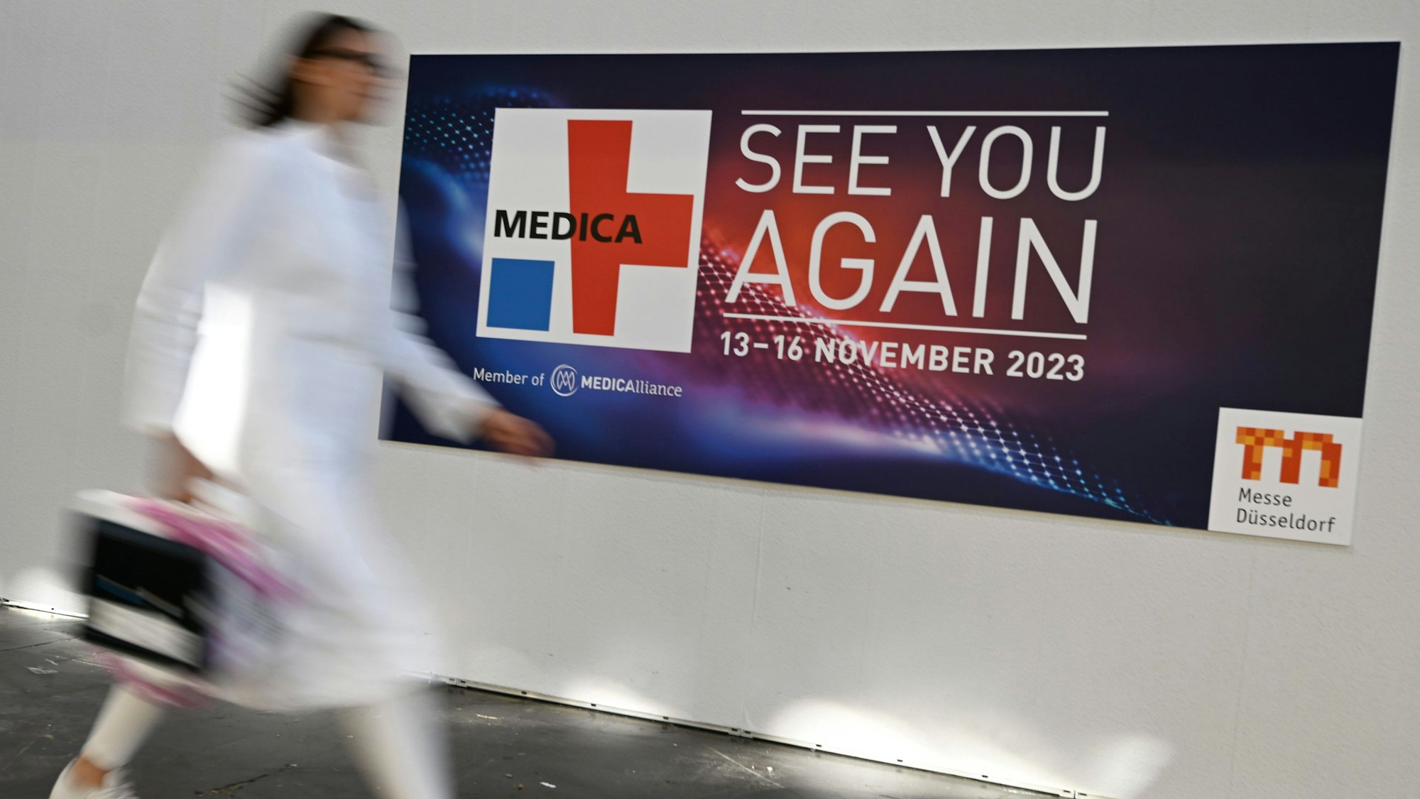 Eine Frau in weißem Kittel eilt an einem Medica-Plakat vorbei.