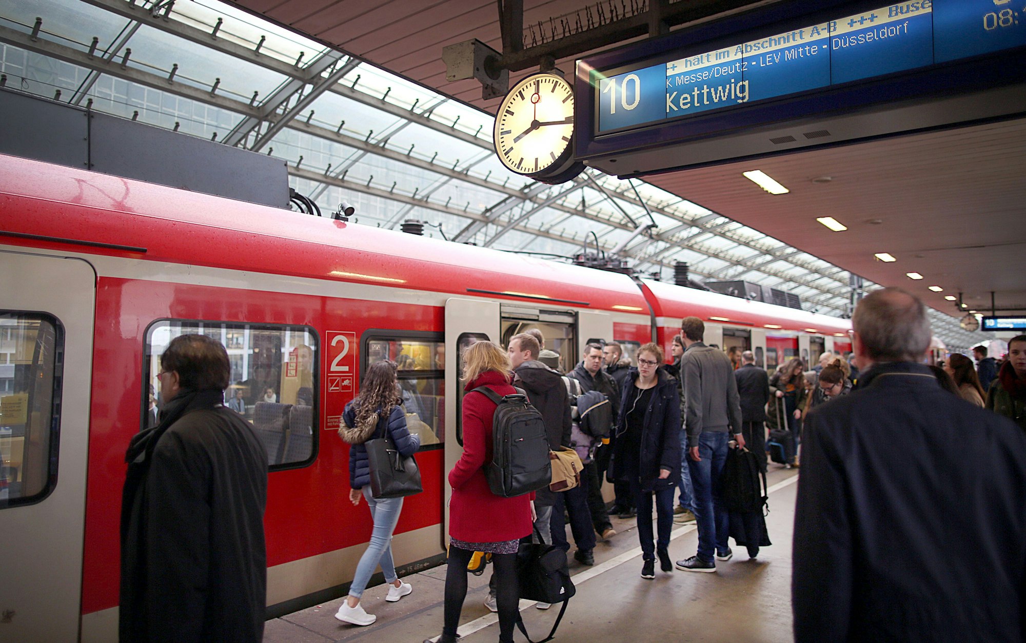 Pendler stehen im Hauptbahnhof Köln vor einer S-Bahn.