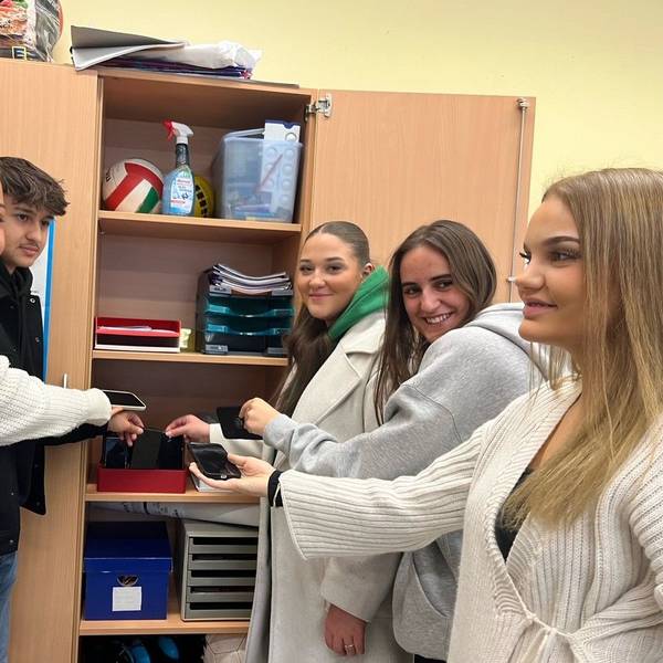 Schülerinnen und Schüler legen ihr Handy in einen Schrank.
