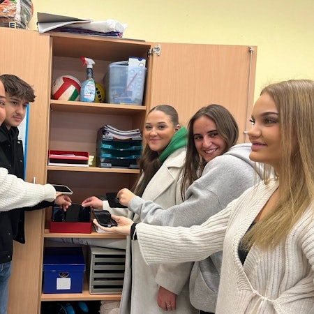 Schülerinnen und Schüler legen ihr Handy in einen Schrank.
