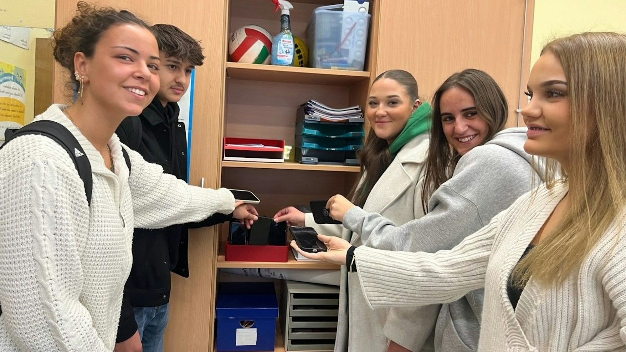 Vier Schülerinnen und ein Schüler demonstrieren, wie sie ihre Handys in einem Schrank verstauen.