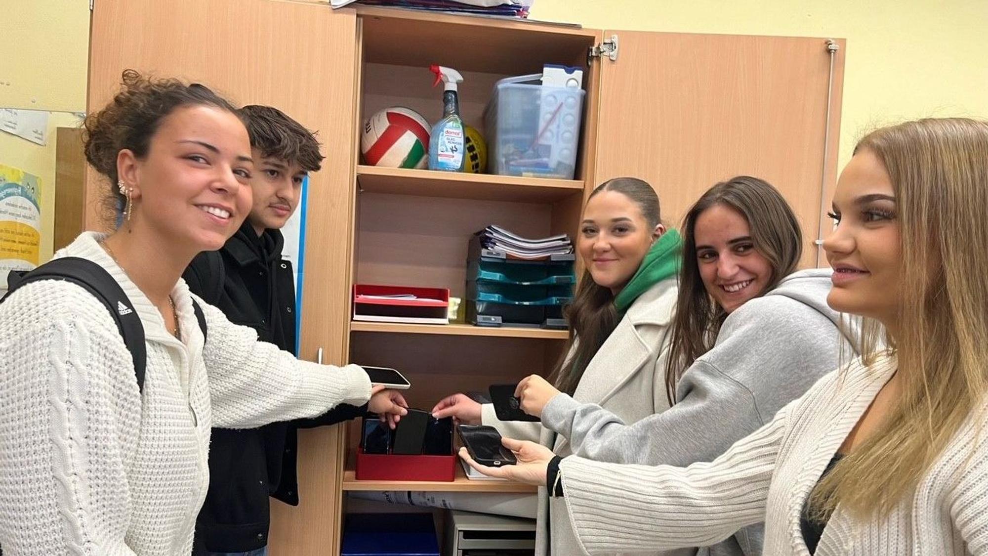 Schülerinnen und Schüler legen ihr Handy in einen Schrank.