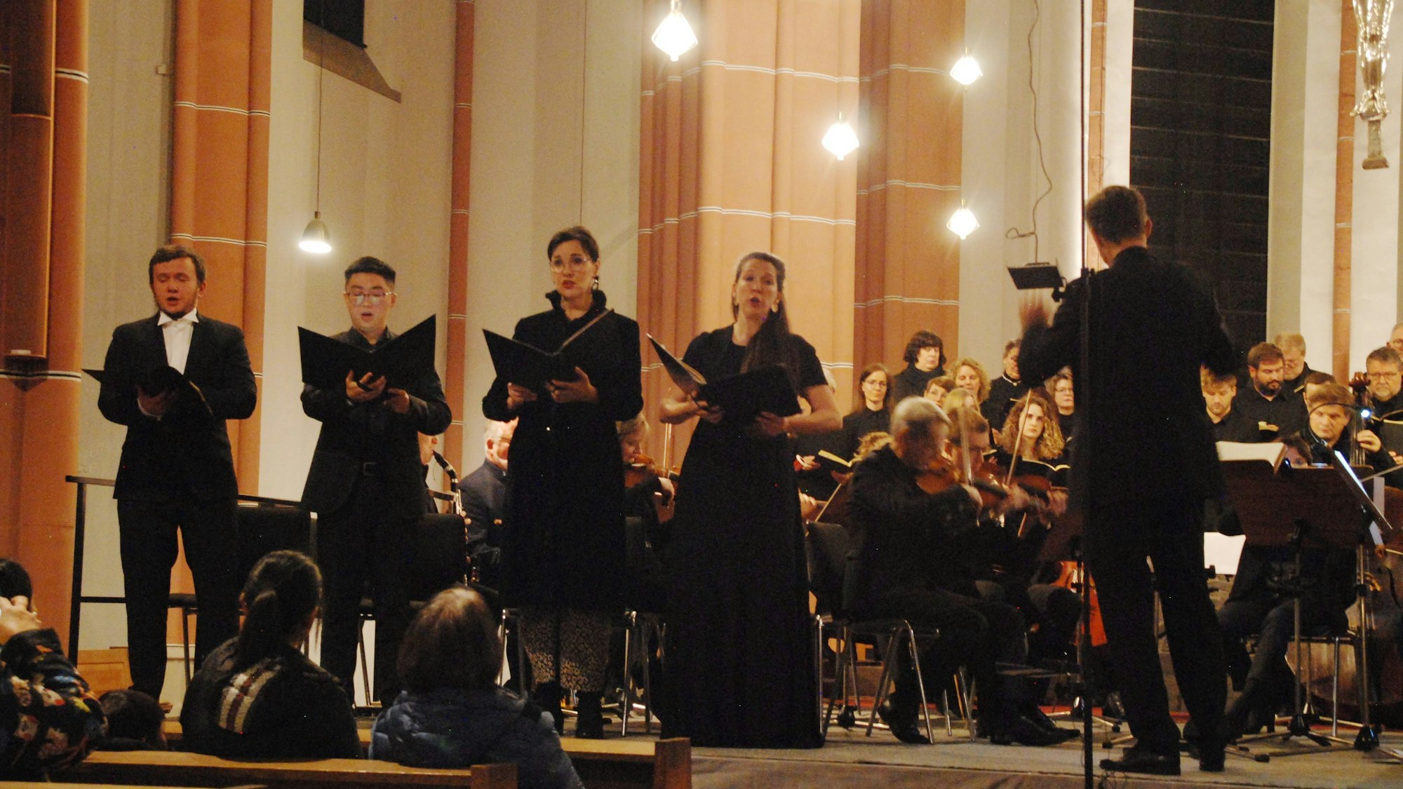 Die vier Sängerinnen und Sänger stehen im Altarraum, zwischen Orchester und Publikum.