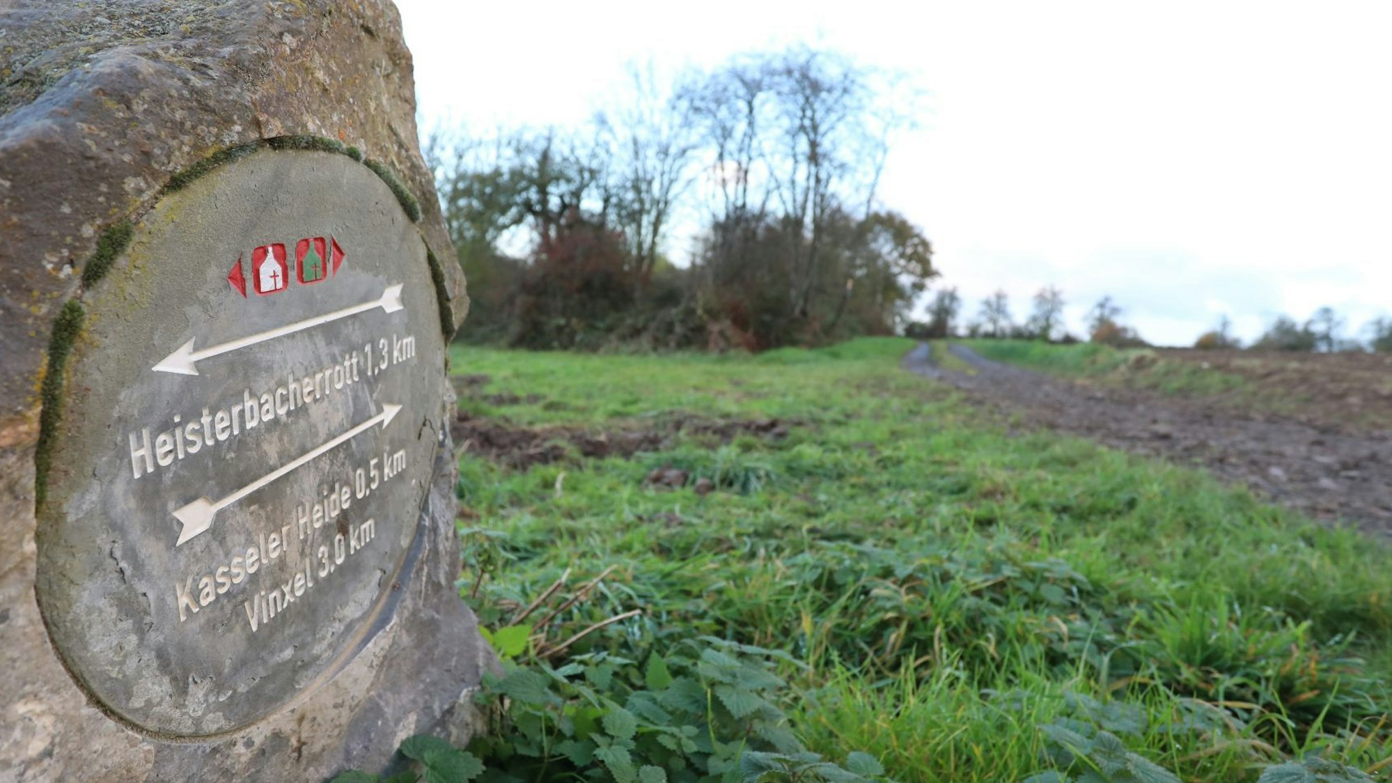 Ein Wegweiser aus Stein neben einem Wanderweg.