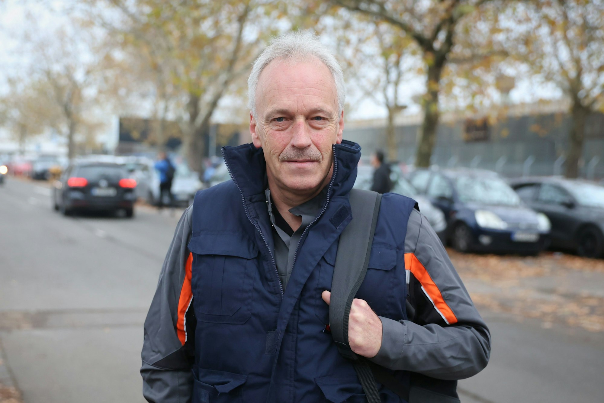 Mann steht mit Rucksack auf Parkplatz.