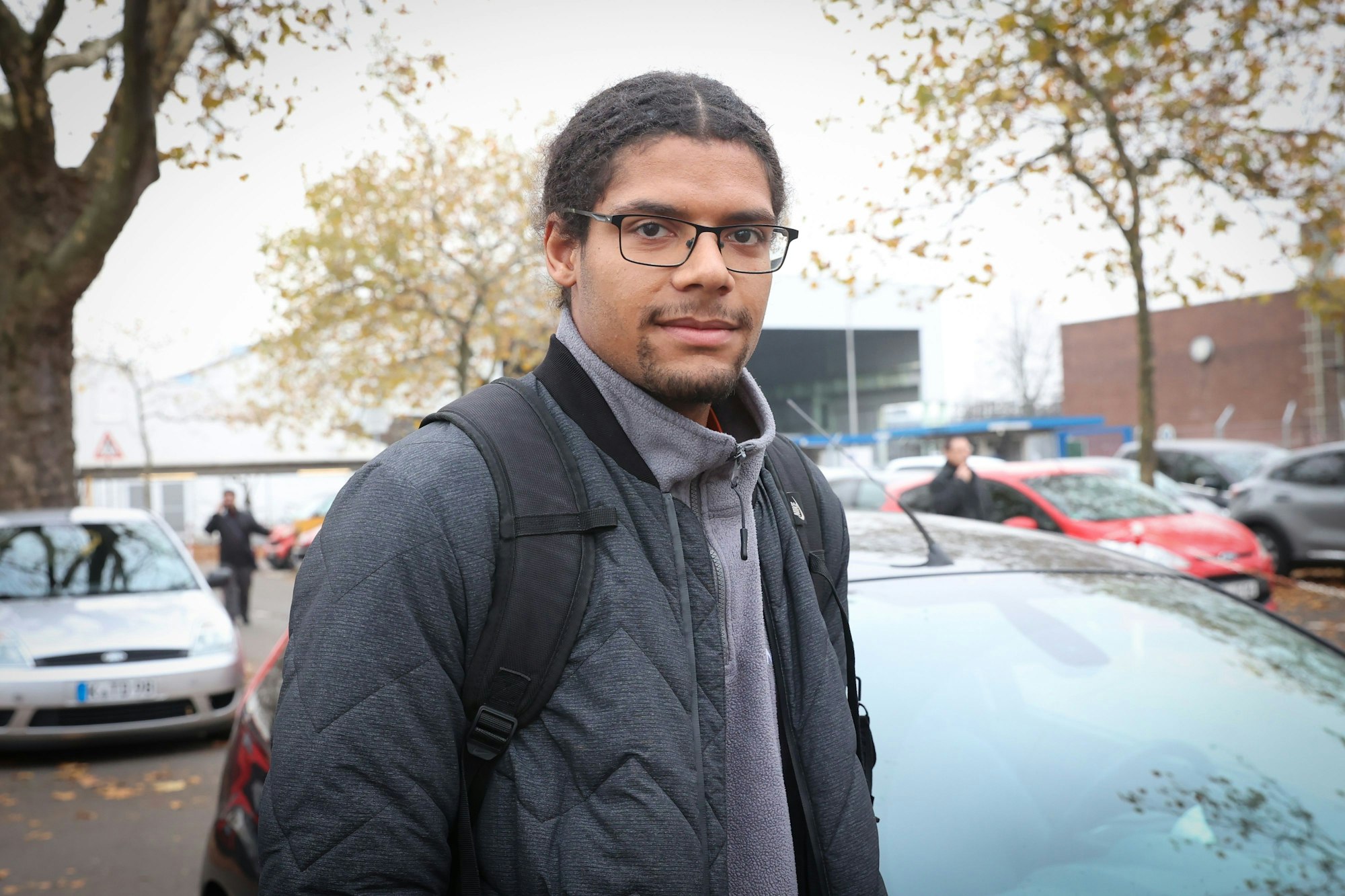 Mann steht zwischen Autos auf Parkplatz.