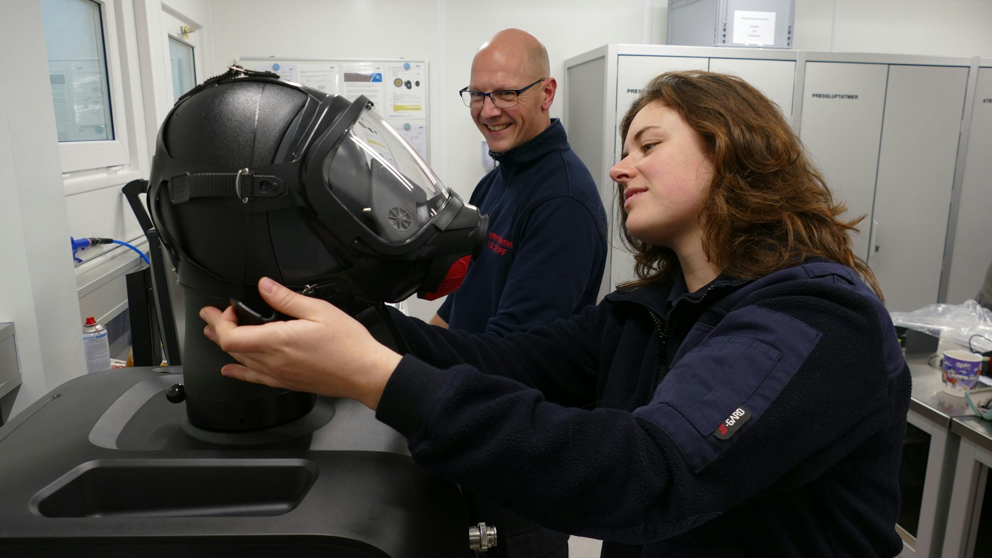 Eine Frau arbeitet an einer Atemschutzmaske, ein Mann sieht ihr zu.
