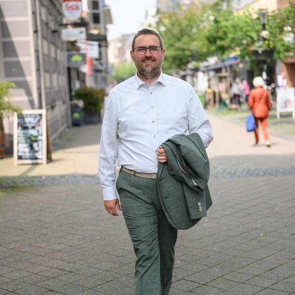 Der Bürgermeister von Dormagen, Erik Lierenfeld, spaziert mit dem Jacket in der Hand und weißem Hemd bei sonnigem Wetter durch die Dormagener Fußgängerzone.