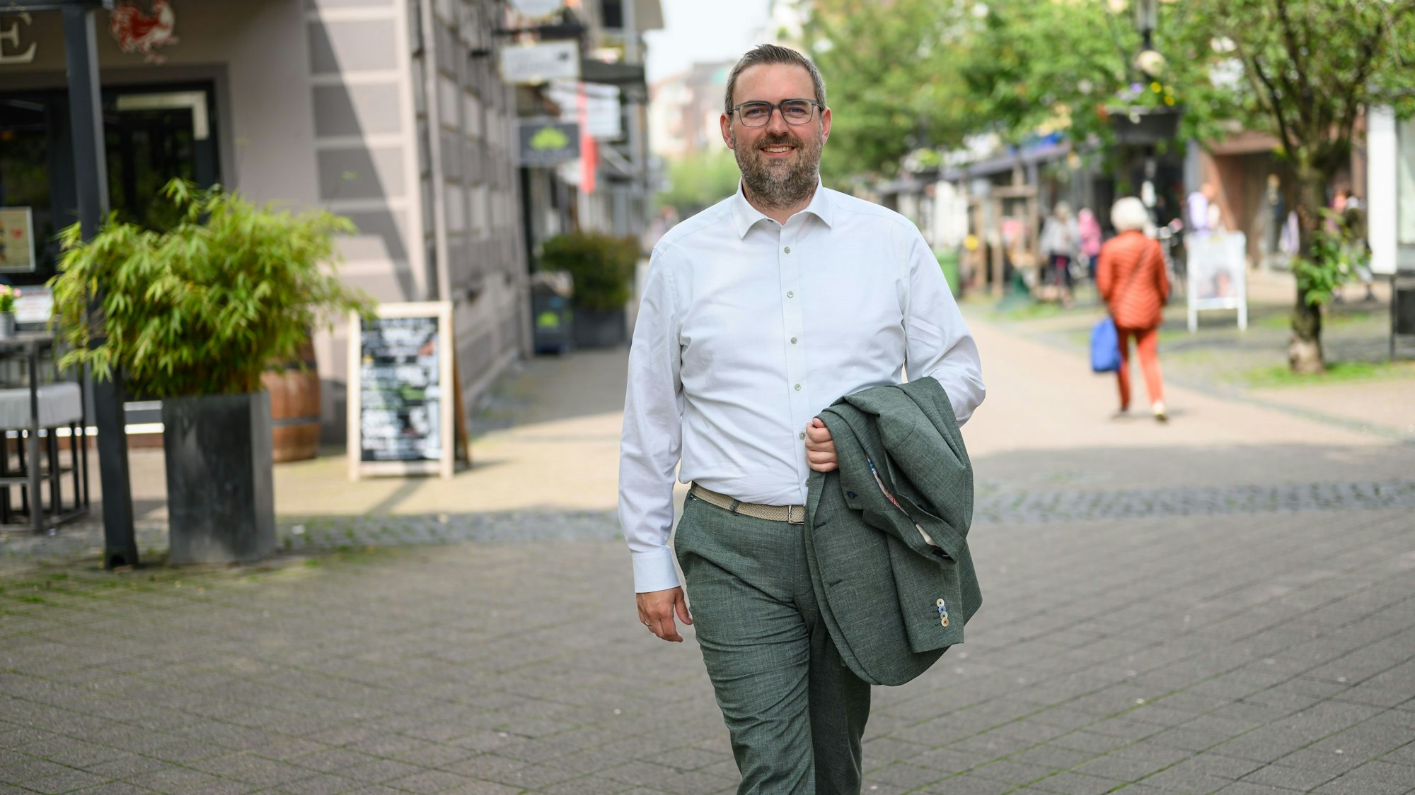 Der Bürgermeister von Dormagen, Erik Lierenfeld, spaziert mit dem Jacket in der Hand und weißem Hemd bei sonnigem Wetter durch die Dormagener Fußgängerzone.