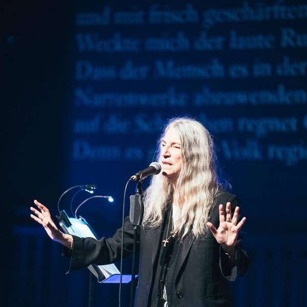 Zu sehen ist die Sängerin Patti Smith auf einer Bühne, vor einem Mikrofon.