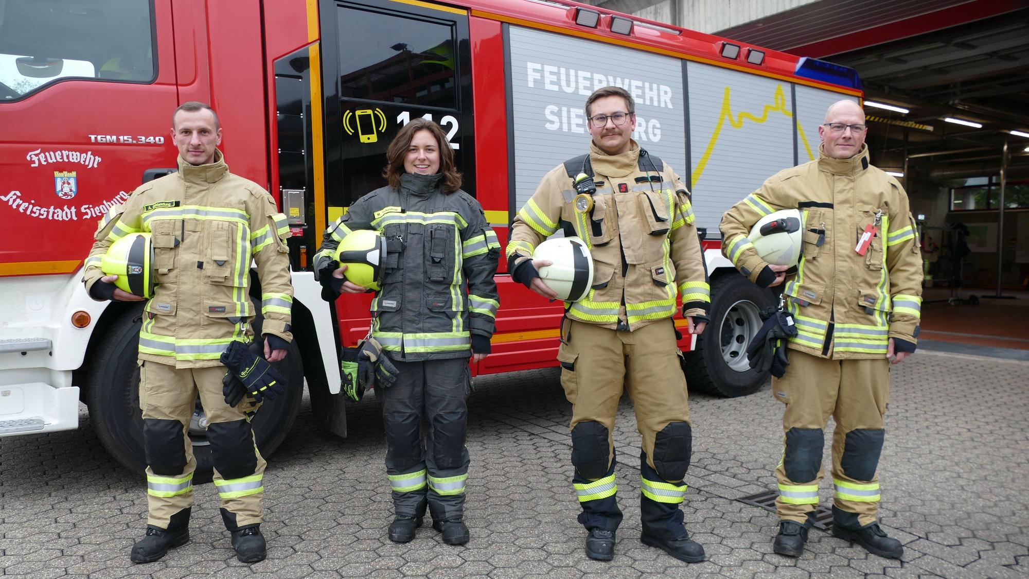 Drei Feuerwehrmänner und eine -frau vor einem Feuerwehrauto.