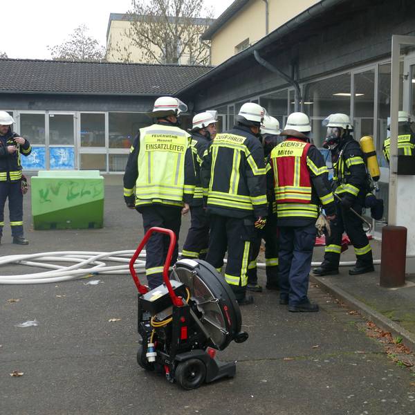 Feuerwehrleute stehen vor dem Eingang des Schulgebäudes.