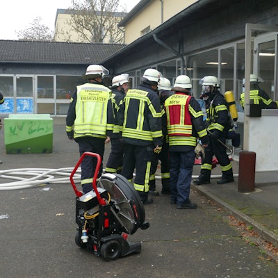 Feuerwehrleute stehen vor dem Eingang des Schulgebäudes.