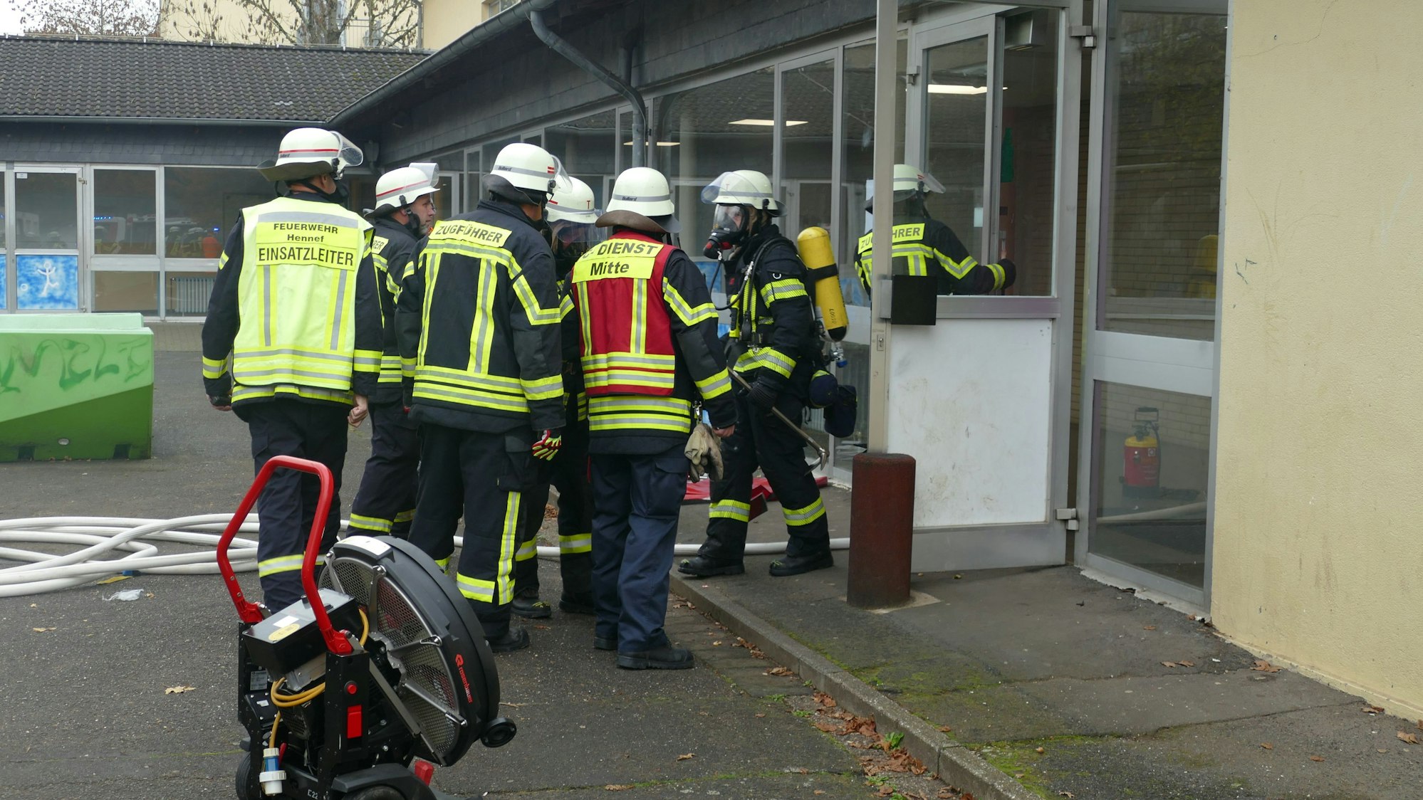 Feuerwehrleute stehen vor dem Eingang des Schulgebäudes.
