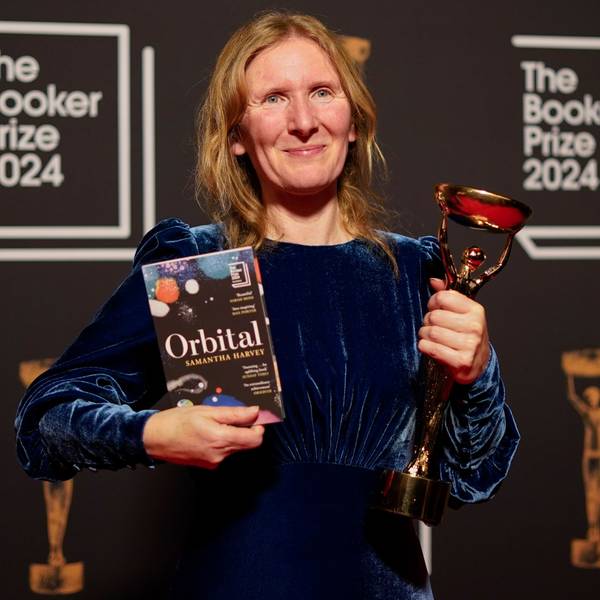 Samantha Harvey hält ihren Roman in der rechten Hand, den Booker-Prize in der linken. Sie trägt ein blaues Samtkleid.