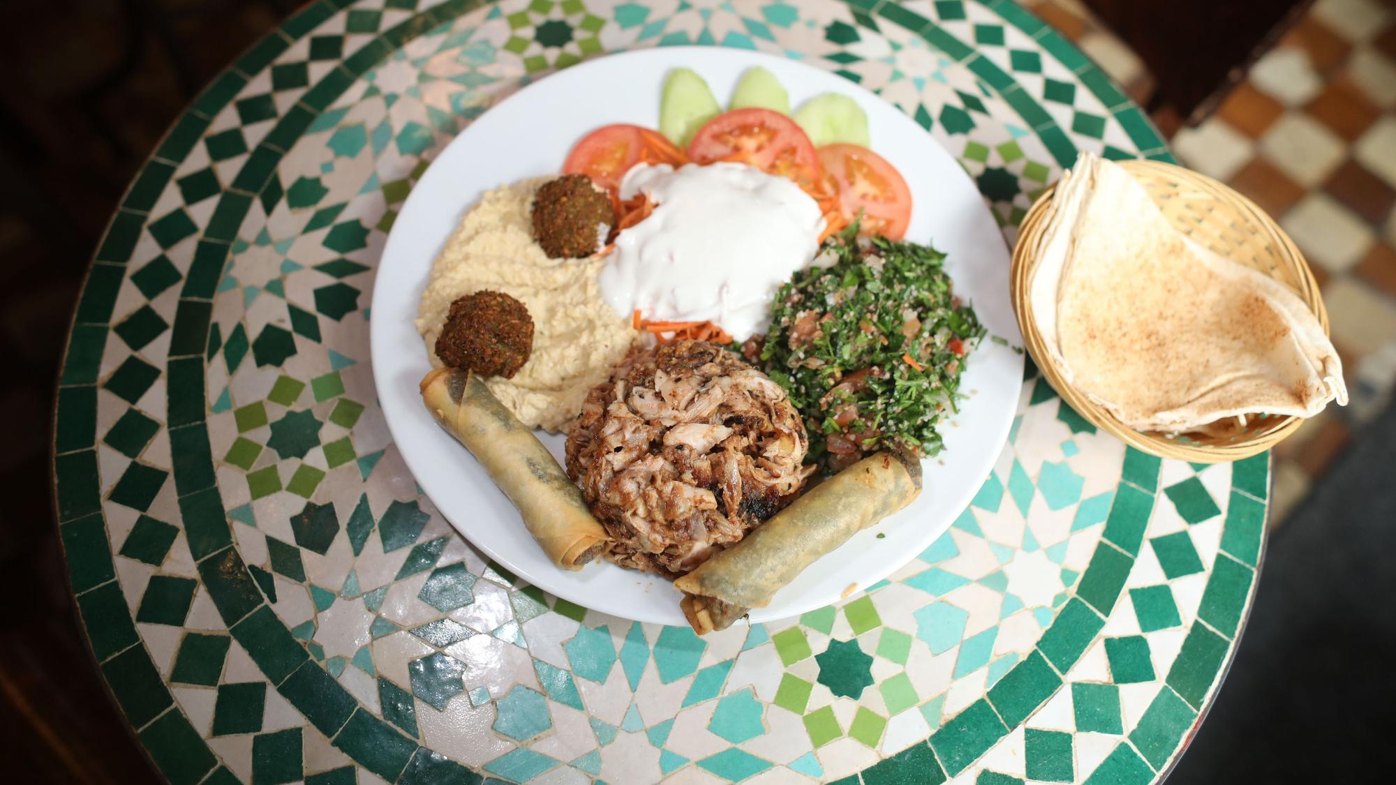 Schawarma, Gemüse, Humus, Blätterteigrollen und Brot sind auf einem Teller angerichtet.