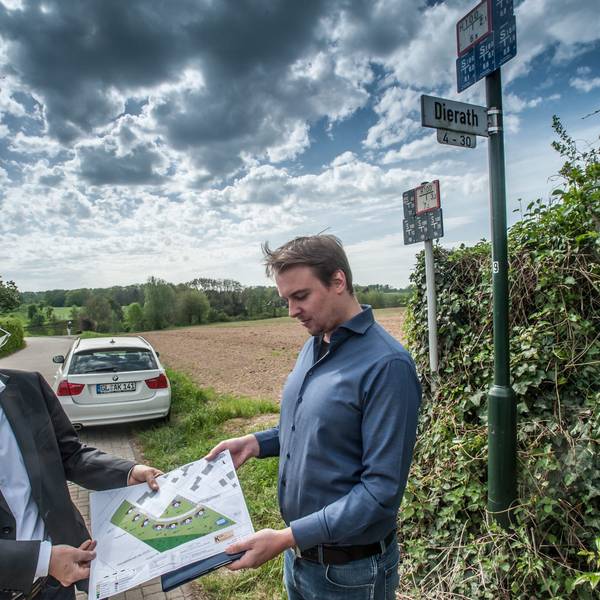 Projektentwickler André Kleinpoppen (l.) und sein Kollege Dominic Loker vor vier Jahren mit dem Bauplan der acht Klimaschutzhäuser vor dem Grundstück in Dierath, das sie erschließen wollen. Es reicht von der Ecke am Straßenschild den Acker hinunter bis zum Waldrand. (Archivbild)