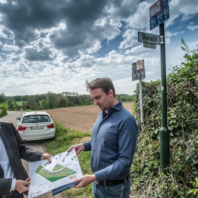 Projektentwickler André Kleinpoppen (l.) und sein Kollege Dominic Loker vor vier Jahren mit dem Bauplan der acht Klimaschutzhäuser vor dem Grundstück in Dierath, das sie erschließen wollen. Es reicht von der Ecke am Straßenschild den Acker hinunter bis zum Waldrand. (Archivbild)