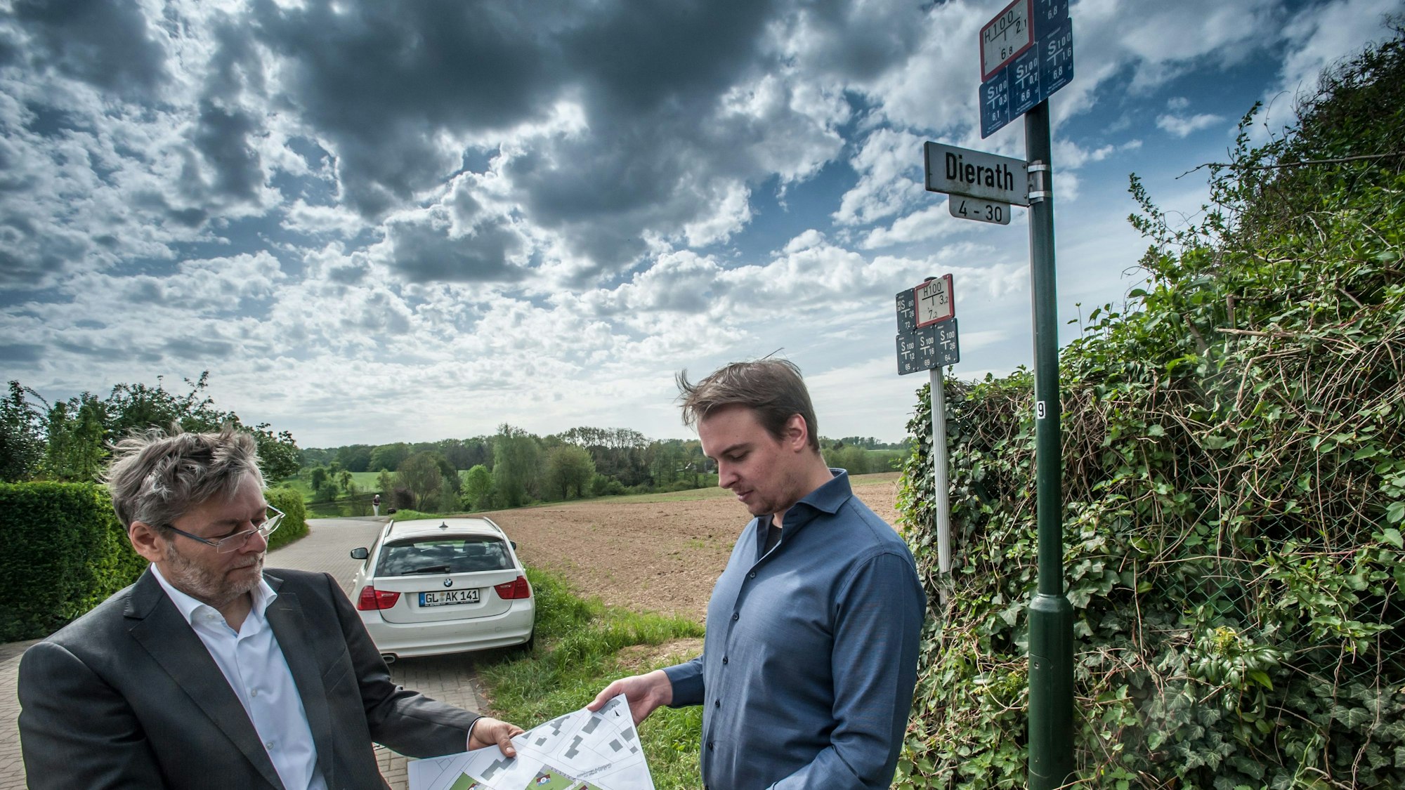 Projektentwickler André Kleinpoppen (l.) und sein Kollege Dominic Loker vor vier Jahren mit dem Bauplan der acht Klimaschutzhäuser vor dem Grundstück in Dierath, das sie erschließen wollen. Es reicht von der Ecke am Straßenschild den Acker hinunter bis zum Waldrand. (Archivbild)