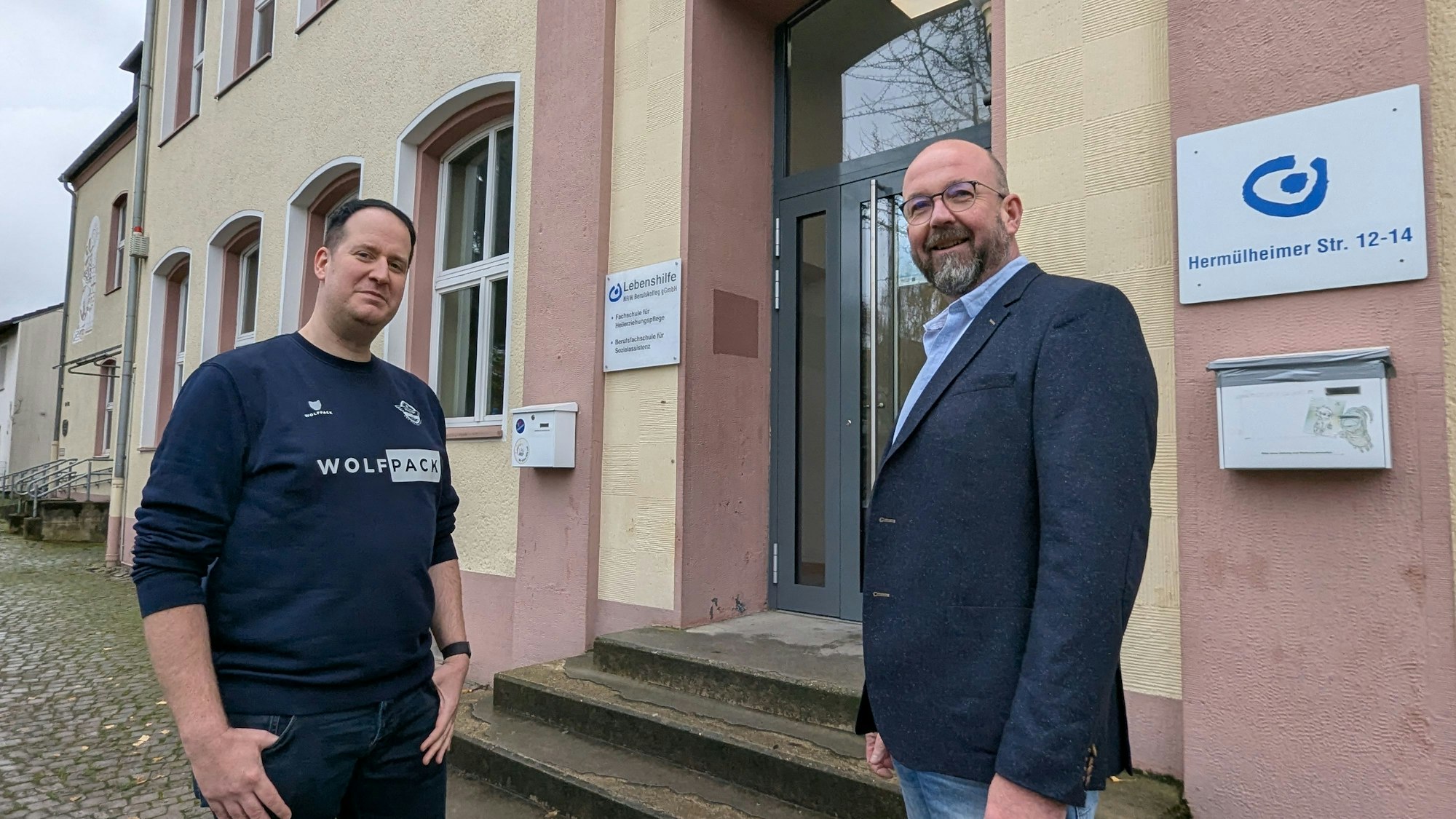 Das Foto zeigt zwei Männer vor dem Eingang zum Berufskolleg im Gebäude der ehemaligen Volksschule.