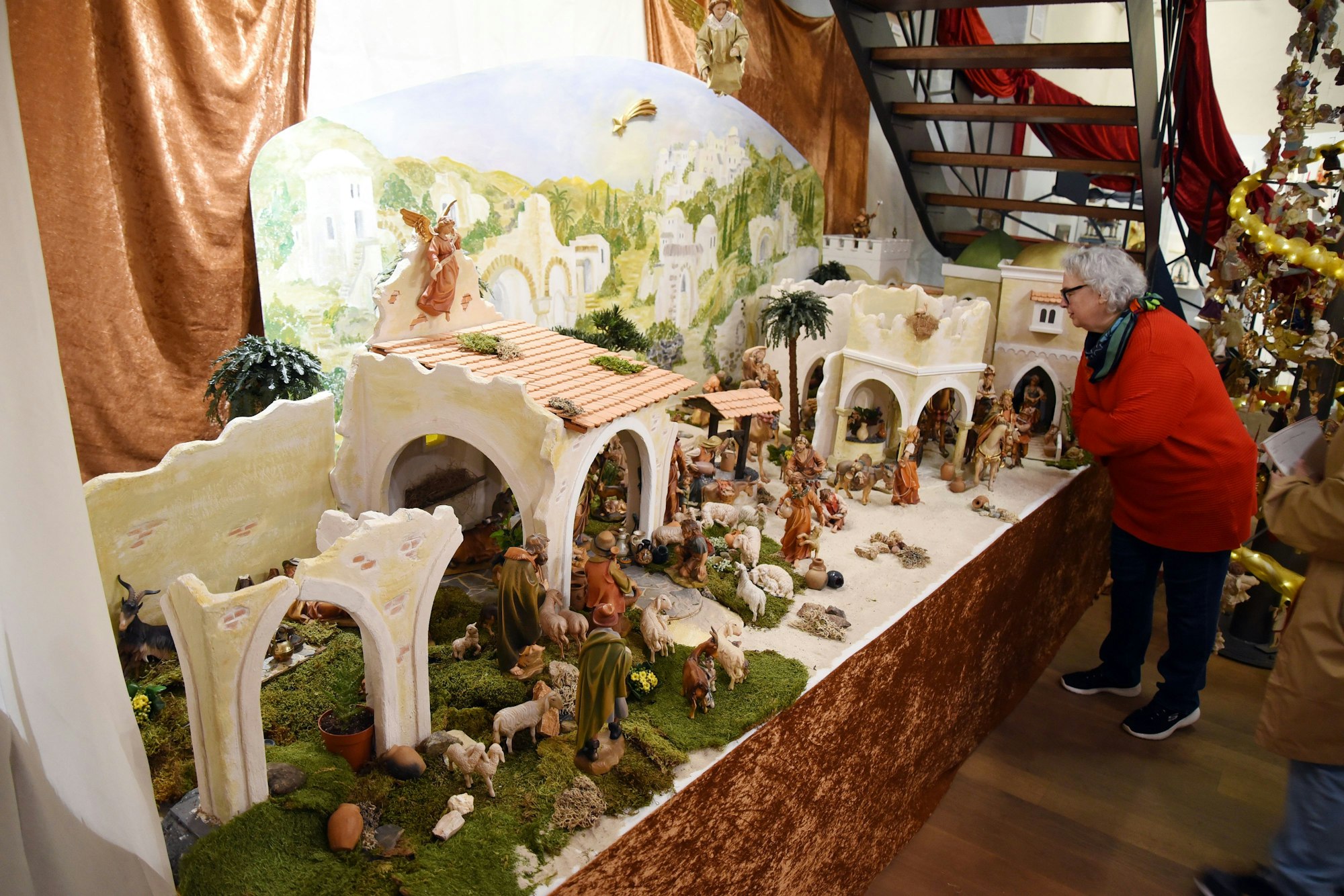 Eine Frau beugt sich über ein Podest, auf dem eine große Krippenlandschaft aufgebaut ist.