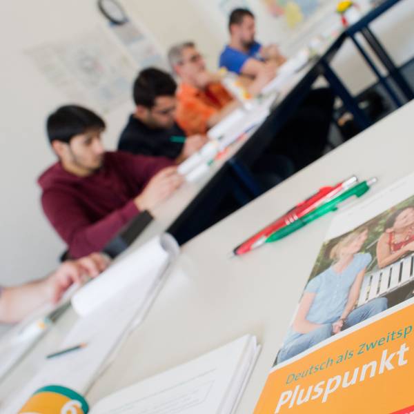 Ein Deutschbuch liegt in einem Integrationskurs. Im Hintergrund sind Kursteilnehmer zu sehen.