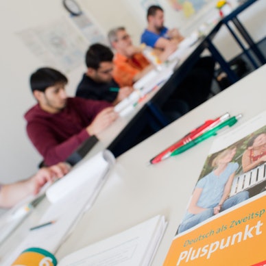 Ein Deutschbuch liegt in einem Integrationskurs. Im Hintergrund sind Kursteilnehmer zu sehen.
