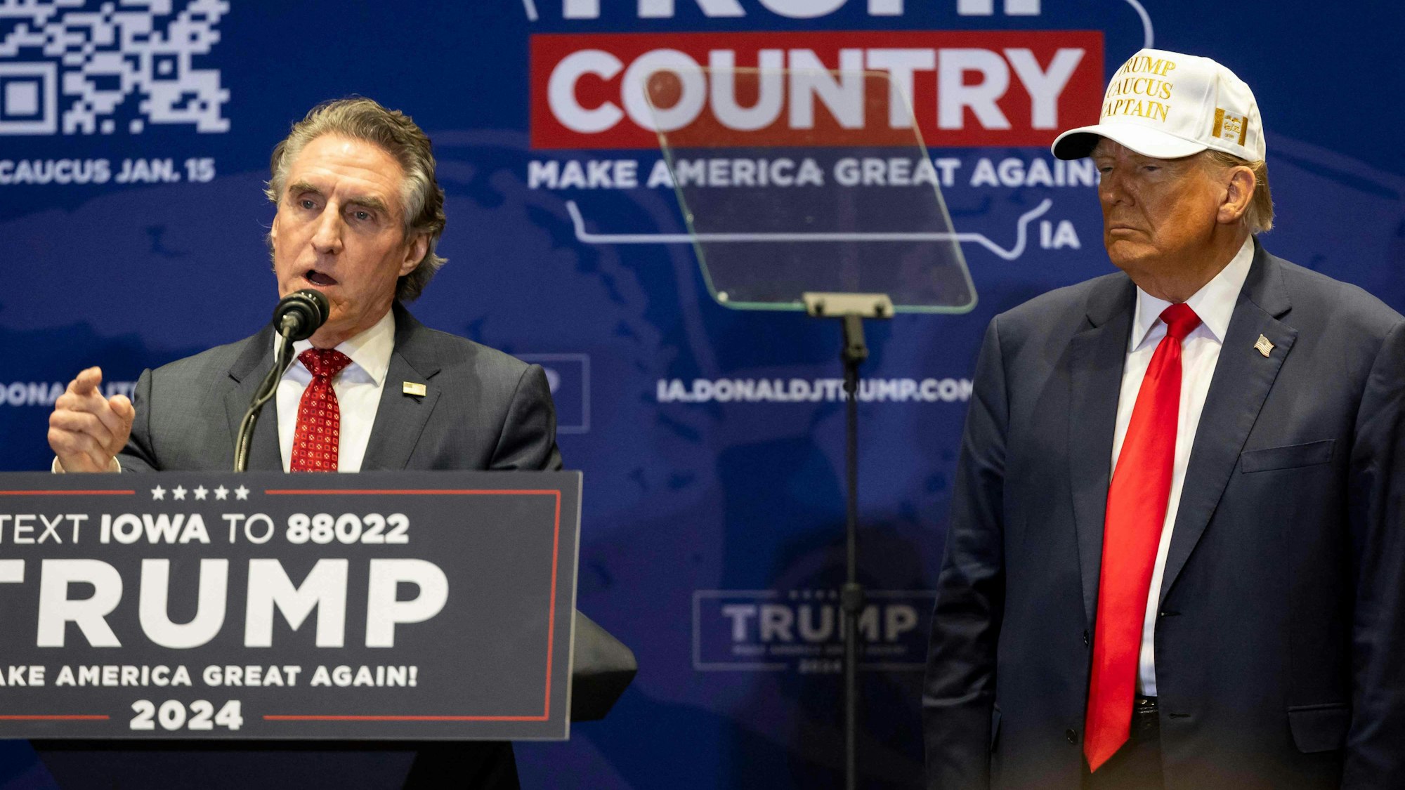 Former US president and Republican presidential hopeful Donald Trump (R) listens as North Dakota Governor Doug Burgum speaks during a "commit to caucus rally" in Indianola, Iowa, on January 14, 2024.