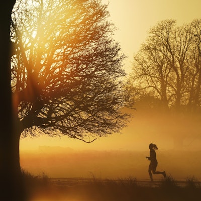 Eine Frau joggt auf einem nebligen Weg, während am Horizont die Sonne aufgeht