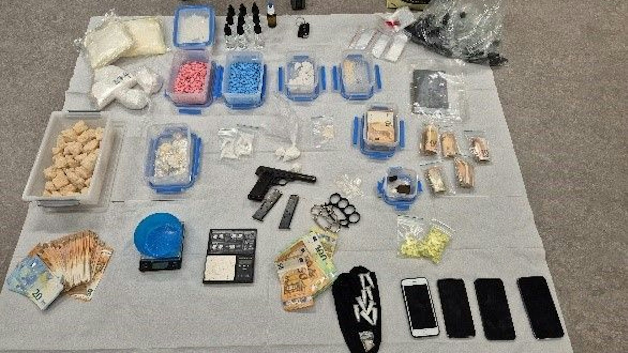 Auf einer Decke sind unter anderem verschiedene Behältnisse mit Drogen, Bargeld, Handys und eine Schusswaffe ausgelegt.