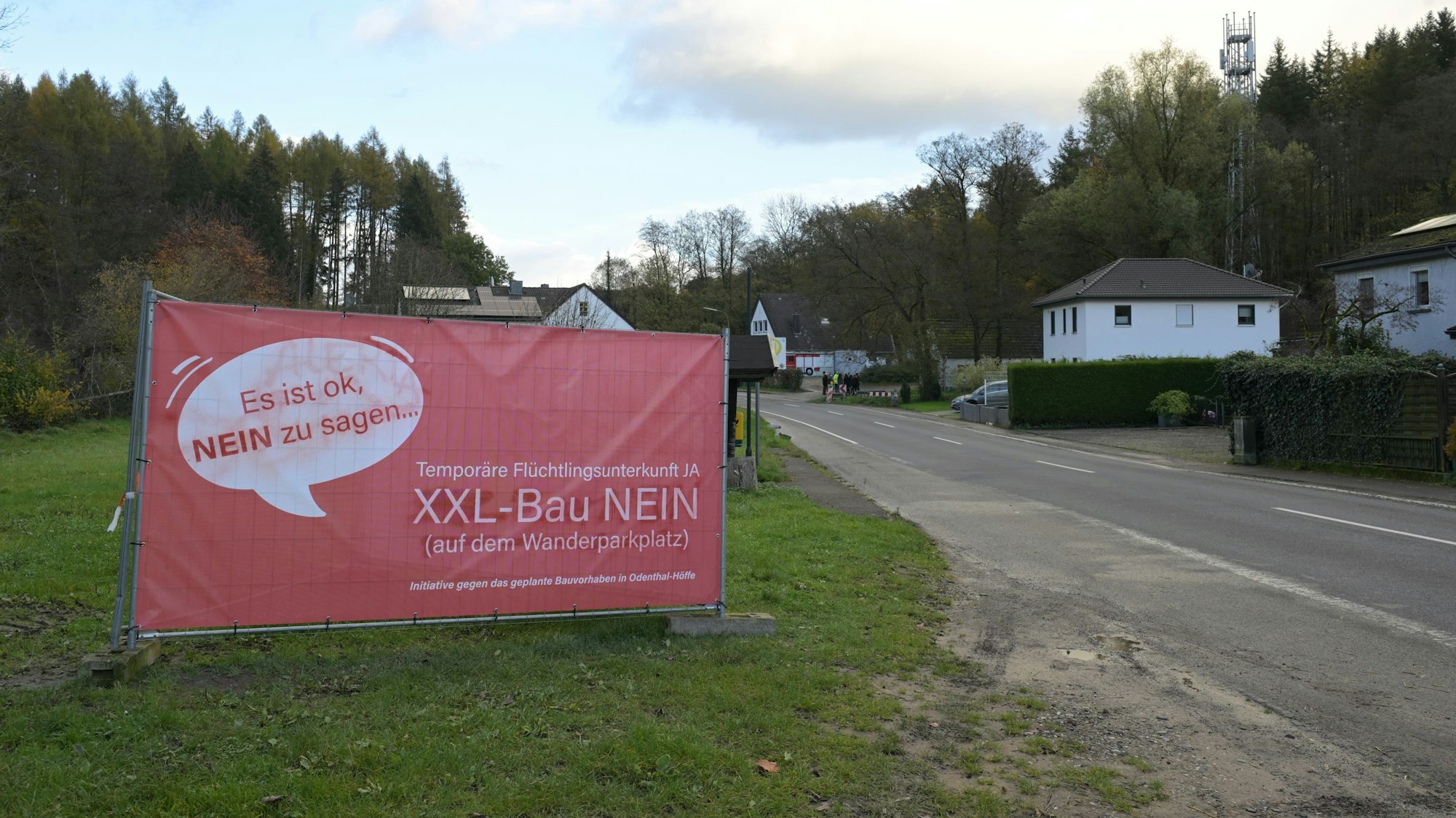 Auf einem roten Plakat am Straßenrand spricht sich eine Bürgerinitiative gegen den Bau eines Flüchtlingsheims in Odenthal-Höffe aus.
