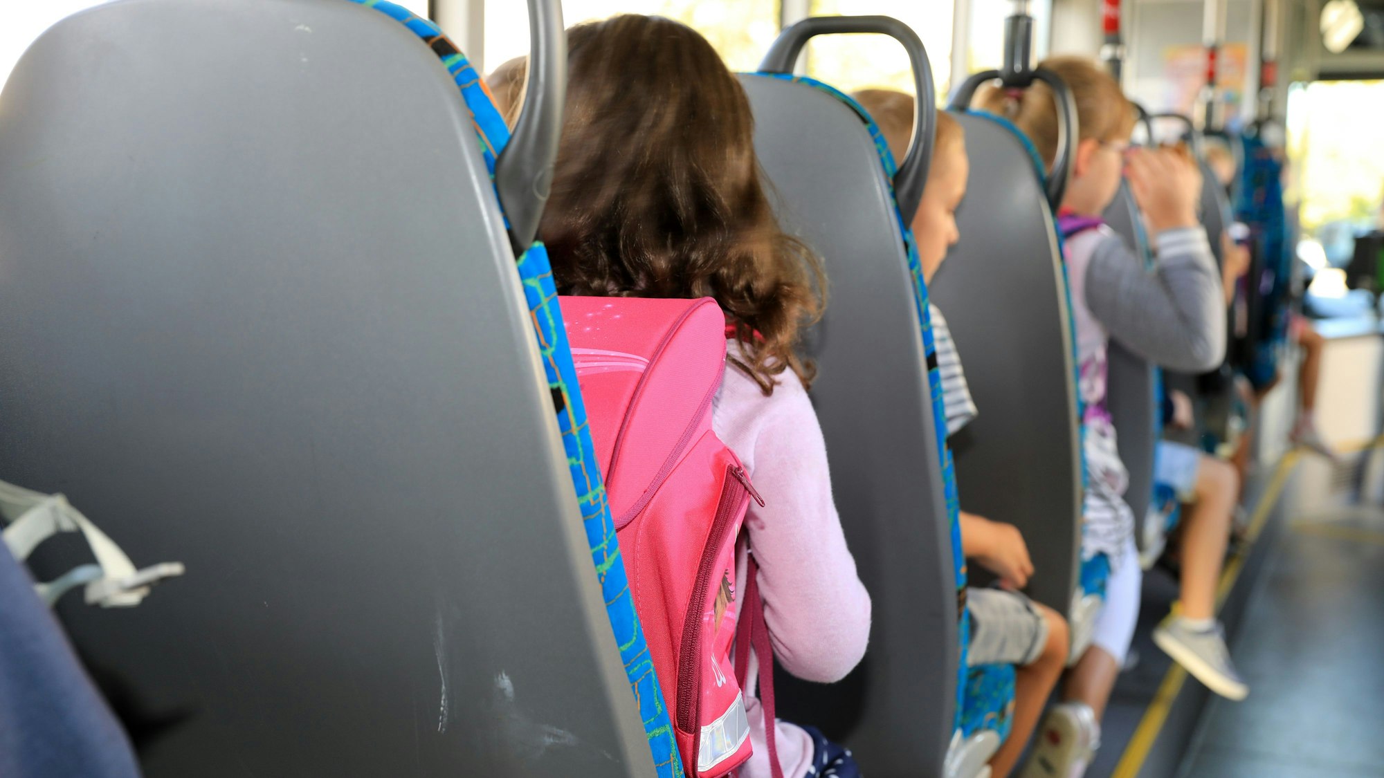 Kinder sitzen mit ihren Ranzen in einem Bus. Sie sind von hinten zu sehen.