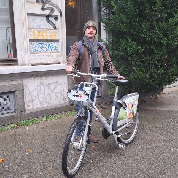 Fabio Botero steht mit einem KVB-Rad auf dem Gehweg.