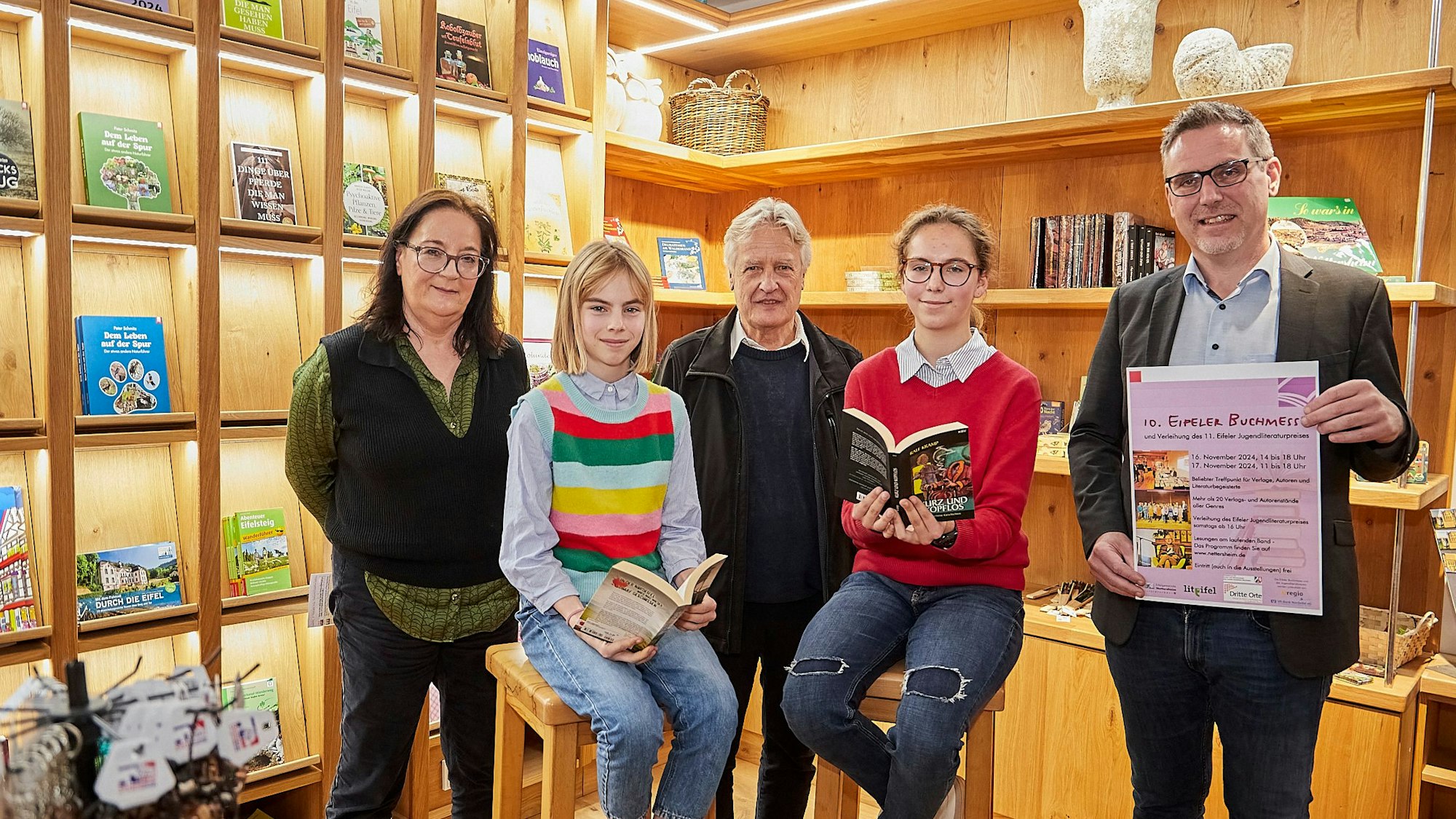 Eine Frau, zwei Jugendliche und zwei Männer stehen beziehungsweise sitzen vor zwei Regalwänden.