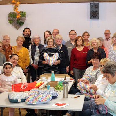 Auf dem Bild ist eine Gruppe von rund 20 Männern und Frauen zu sehen, die Herzkissen für Brustkrebspatienten genäht haben.