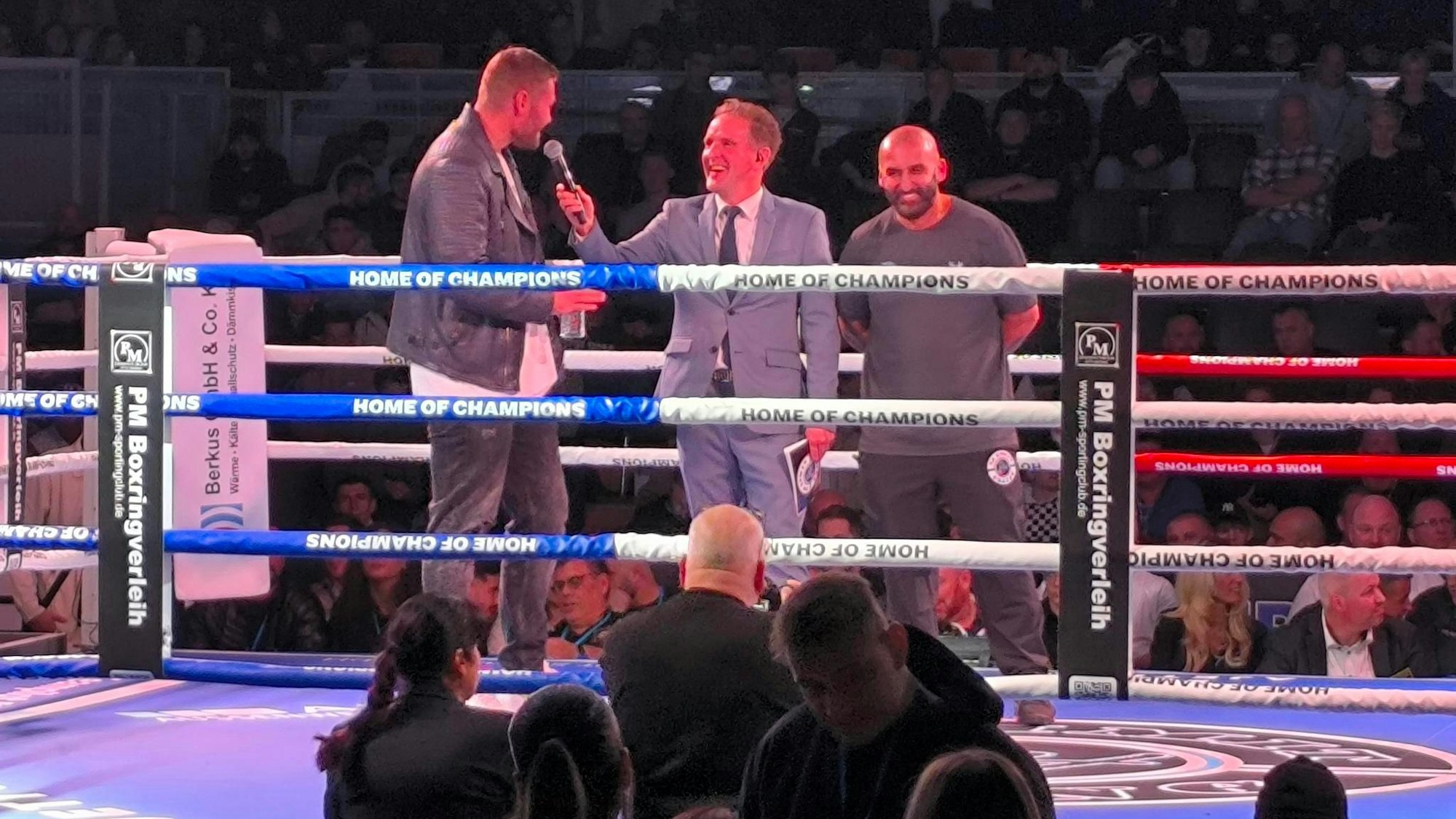 Tom Schwarz (l.) im Interview mit Ringsprecher Ingo Rohrbach (m.). Trainer und Veranstalter Bekim Hoxhaj (r.) zeigt sich amüsiert.