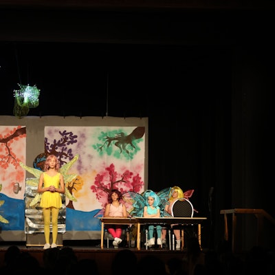 Kinder stehen und sitzen in Engelskostümen auf einer Bühne.