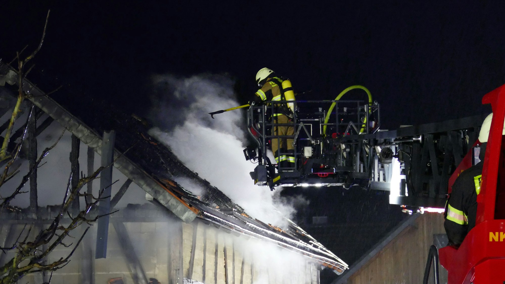 Ein Feuerwehrmann im Dreileiterkorb über einem brennenden Gebäude.