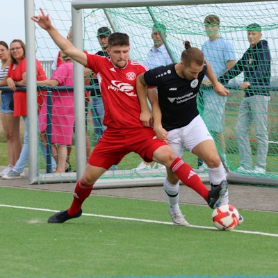 Ein Fußballer erobert mit einem langen Bein an der Außenlinie den Ball von einem Gegenspieler.