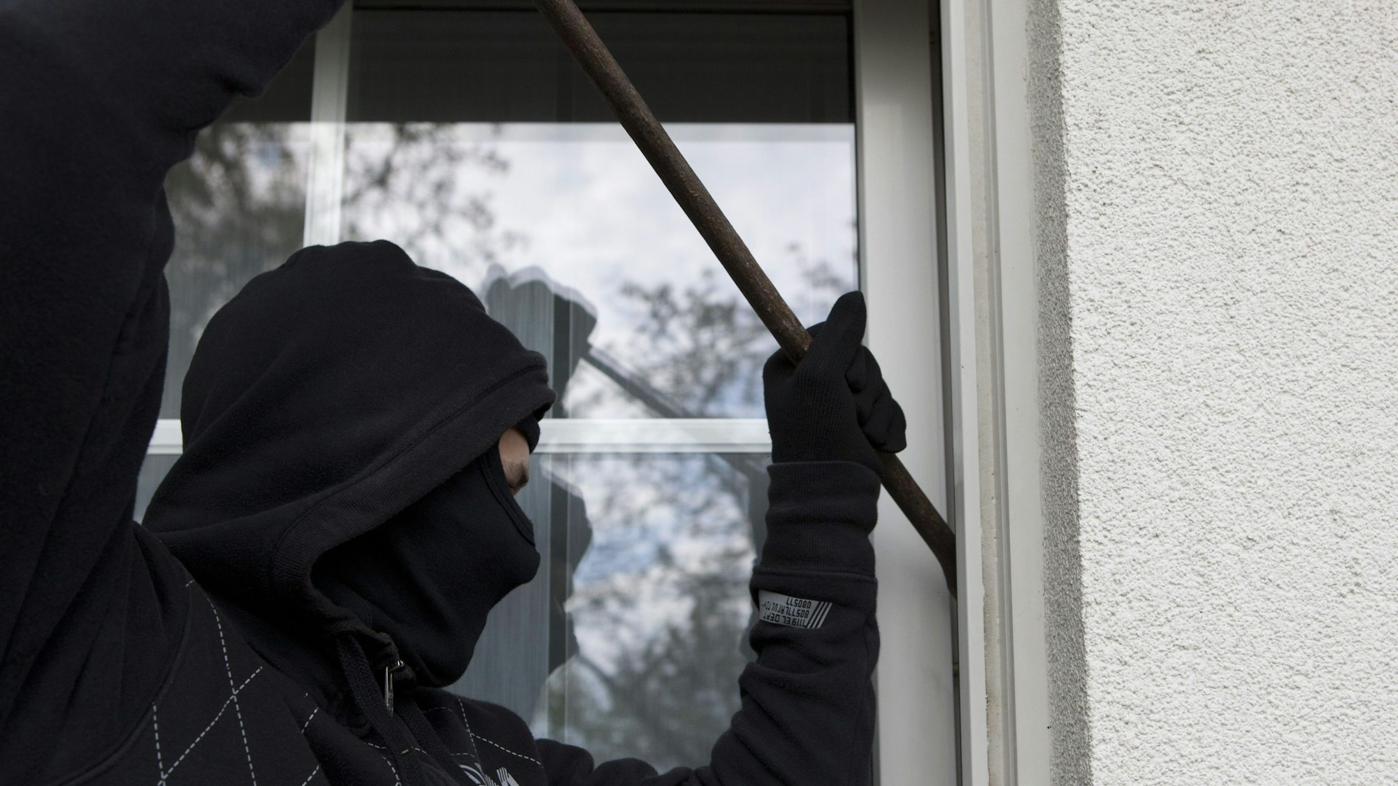 Ein vermummter Mann hebelt eine Terrassentür auf.