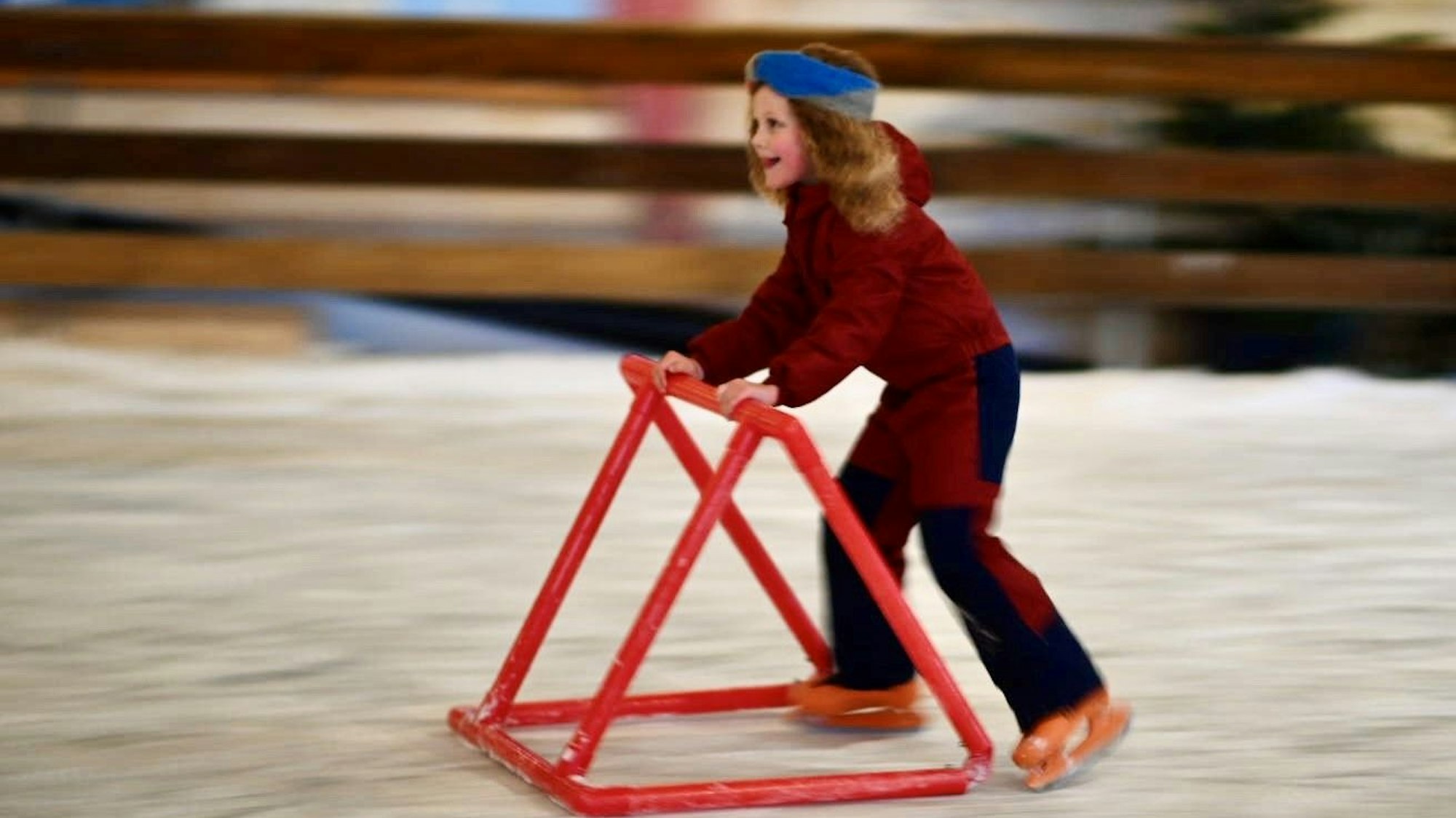 Das Bild zeigt ein Mädchen, das mithilfe einer Rutschhilfe Schlittschuh läuft.